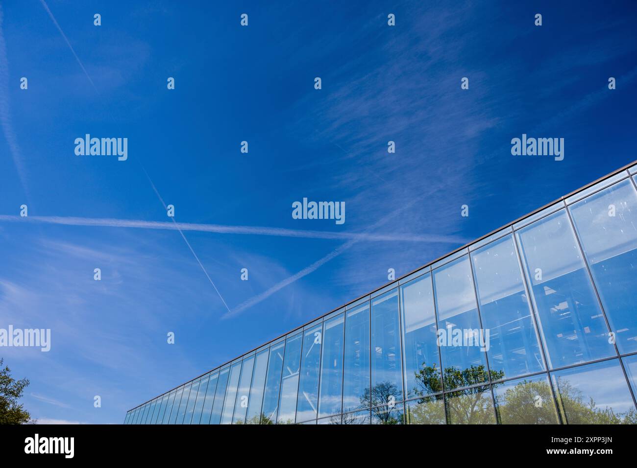 Traînées de condensation dans le ciel bleu. au premier plan un bâtiment industriel avec une façade vitrée Banque D'Images