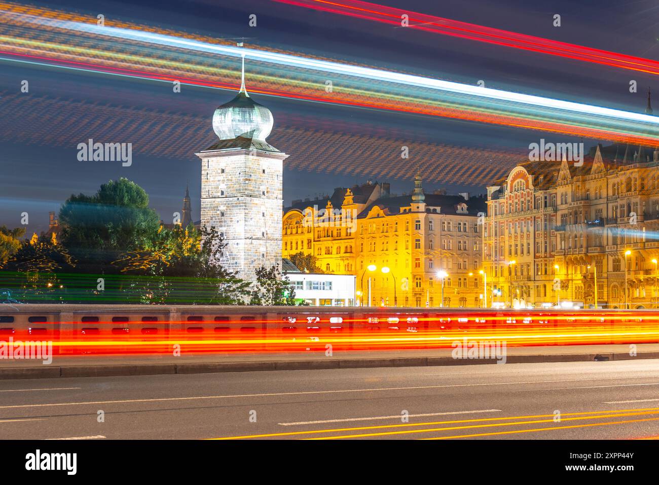 Une photographie longue exposition capture les lumières vibrantes de Prague au crépuscule, mettant en valeur le château d'eau de Sitkov et le quai Masaryk. Des traînées de circulation éclairent la route devant les bâtiments. Banque D'Images