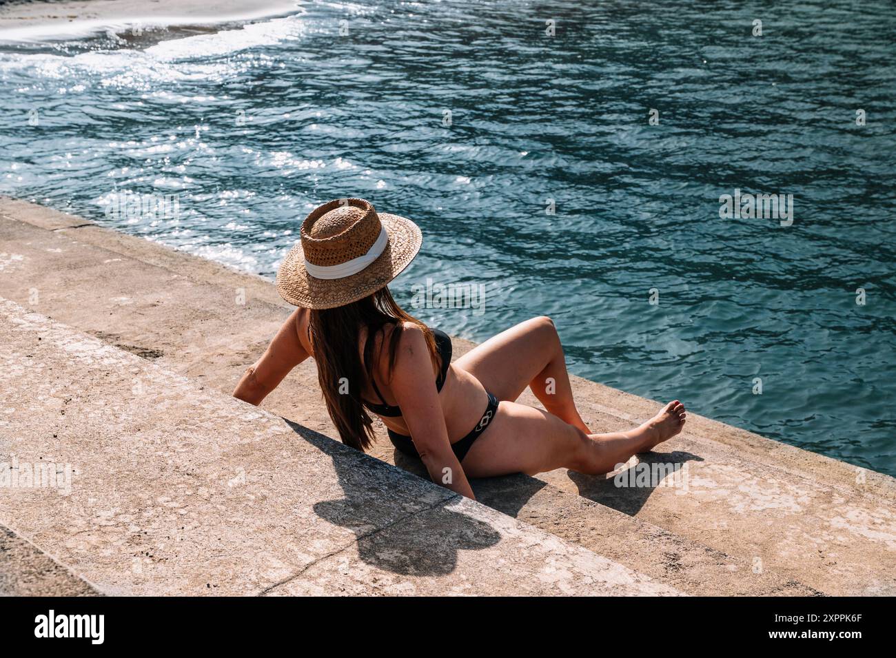 Femme assise sur le Malecon bronzer en bikini avec un chapeau à côté de la plage. Banque D'Images