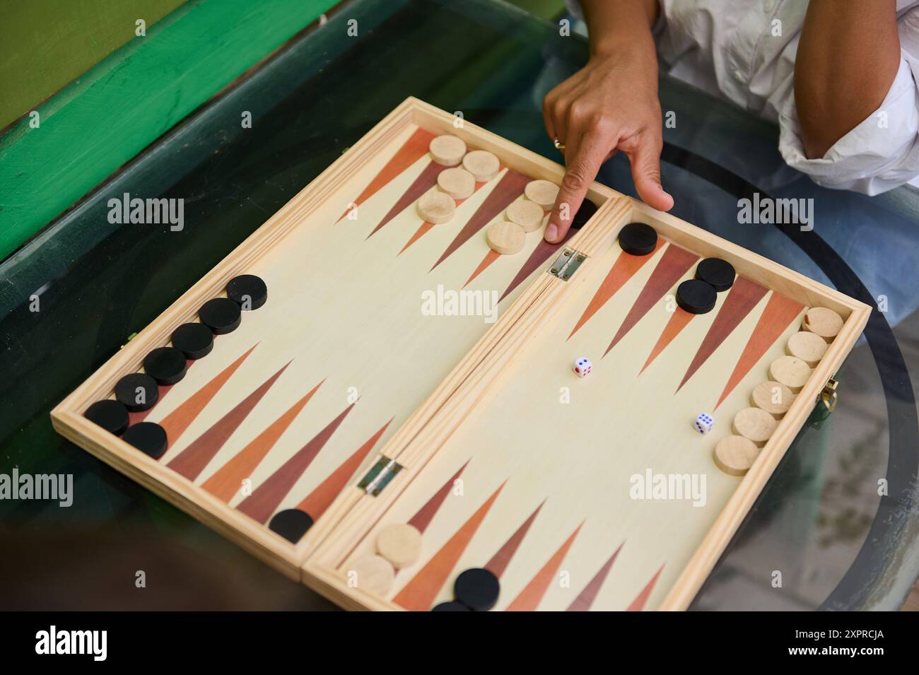 Une image en gros plan montrant des gens jouant au backgammon sur une planche de bois, avec des mains déplaçant des morceaux et des dés en vue. Idéal pour illustrer la stratégie, lei Banque D'Images