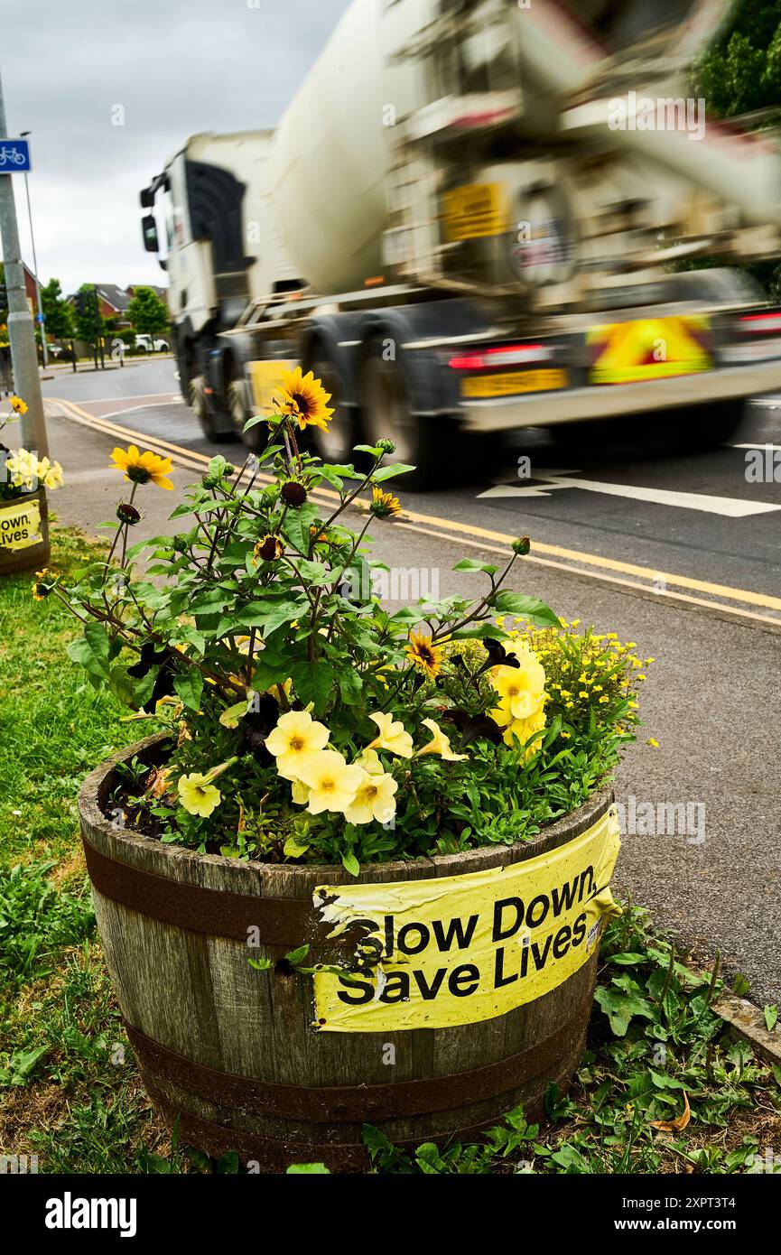 Mélangeur à béton passant le planteur floral montrant à la circulation venant en sens inverse une affiche Slow Down Save Lives Banque D'Images