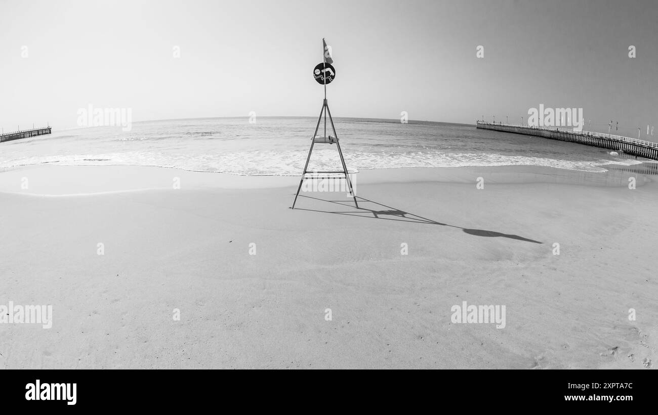 Plage océan pas de gens calmer les eaux de mer calmes avec balise de nage de sauveteur vers l'horizon de la mer entre jetée de jetée est un paysage blanc noir. Banque D'Images