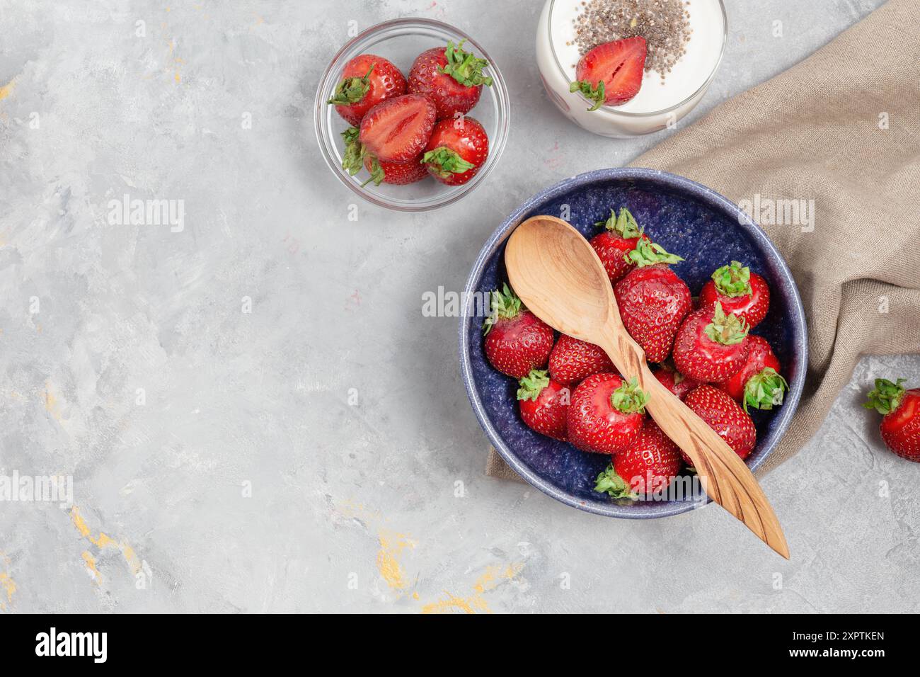 Vue de dessus de fraises fraîches dans un bol bleu avec une cuillère en bois, accompagné d'un verre de yaourt garni de graines de chia. Banque D'Images