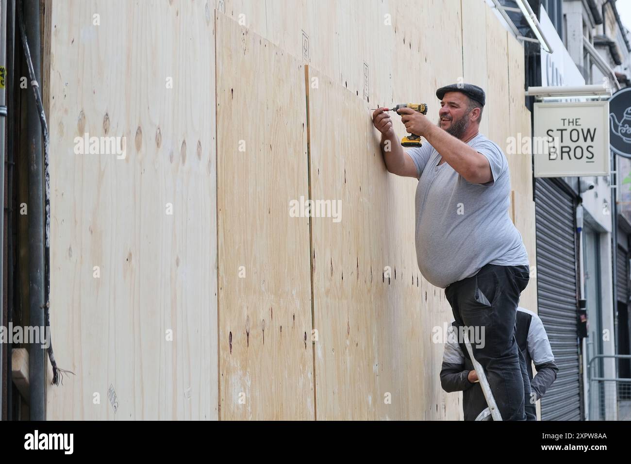 Londres, Royaume-Uni, 7 août 2024. Un travailleur monte à bord d'un magasin alors que les commerces ferment tôt avant une éventuelle manifestation d'extrême droite contre l'immigration et une contre-manifestation antiraciste prévue à Walthamstow. Une liste de 39 bureaux de soutien à l'immigration et d'avocats a été diffusée sur les médias sociaux pour encourager les manifestations aux adresses fournies. Crédit : onzième heure photographie/Alamy Live News Banque D'Images