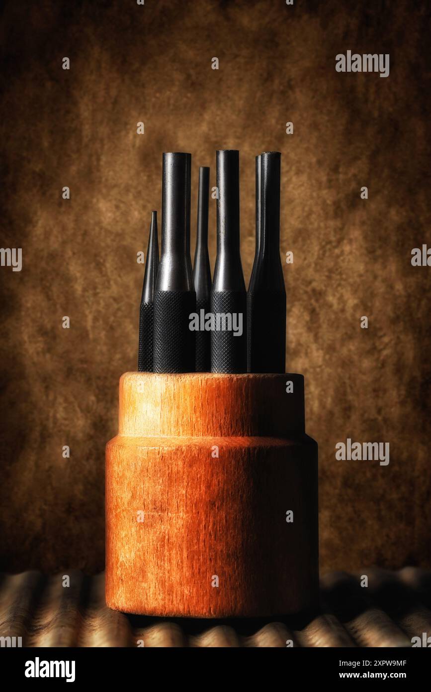 Outils encore de la vie. Un poinçon antique fixé dans son support en bois sur une surface métallique ondulée et fond marbré. Banque D'Images