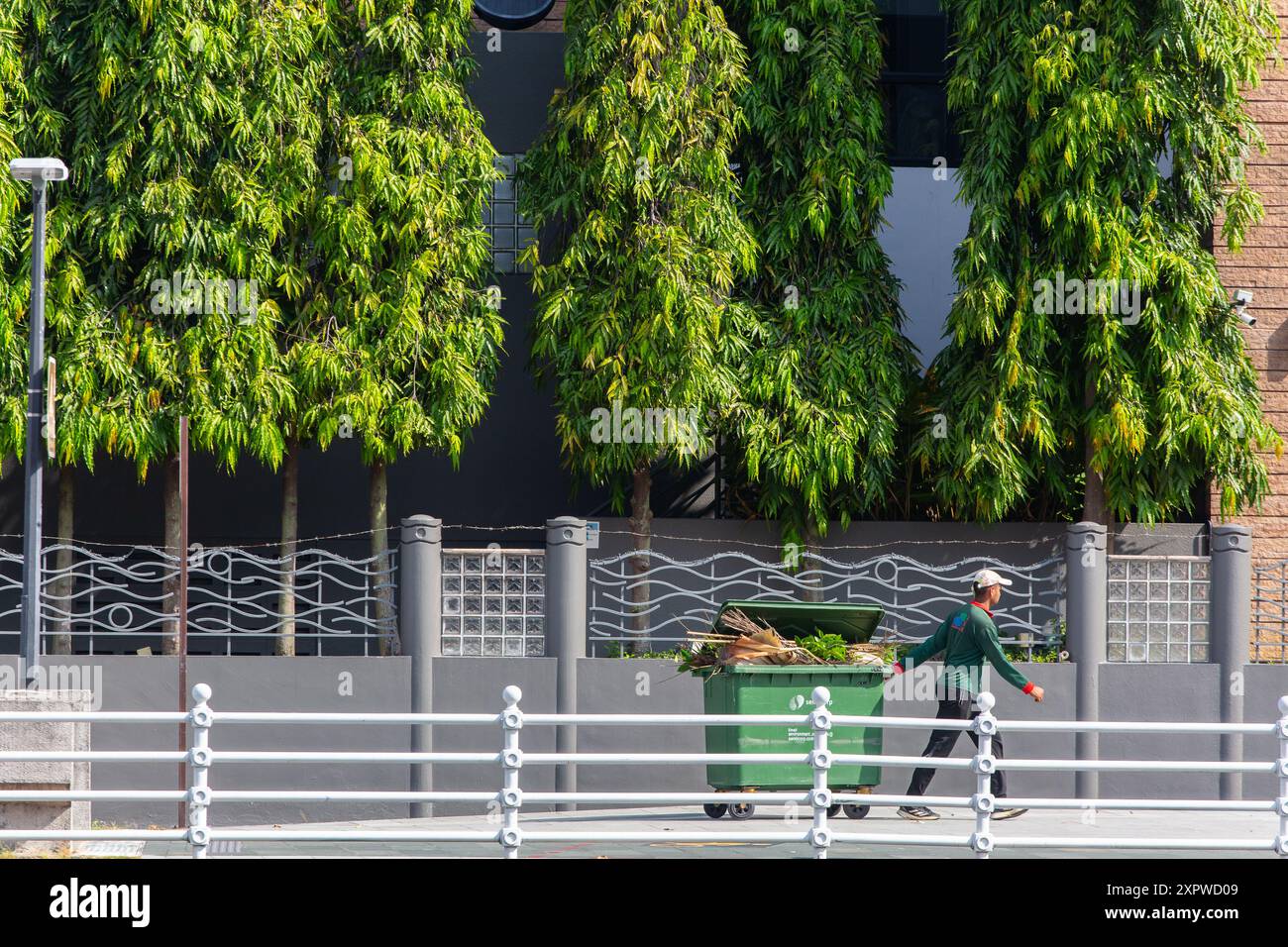 Un nettoyeur public tire la goulotte à ordures avec des roues pour jeter les déchets remplis à l'intérieur. Singapour. Banque D'Images
