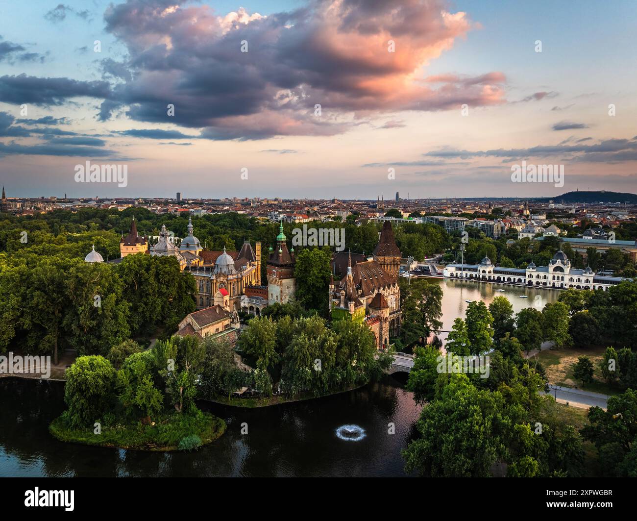 Budapest, Hongrie - vue aérienne du parc municipal et du lac (Varosligeti to) avec le château de Vajdahunyad au coucher du soleil. Feuillage vert, ciel de coucher de soleil spectaculaire et nuages Banque D'Images