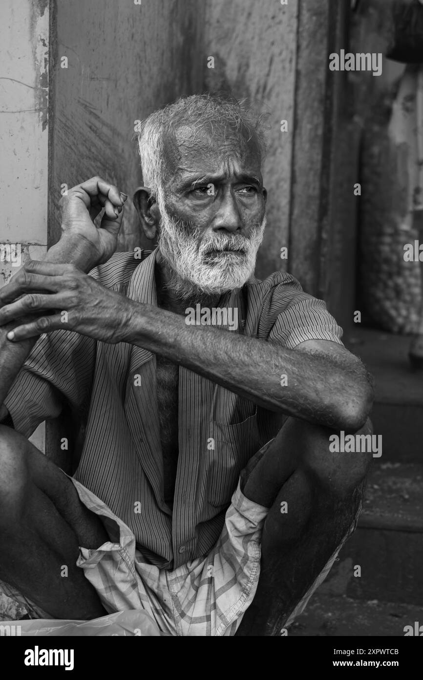 Vieux pauvre indien senior non identifié avec un visage ridé brun foncé, des cheveux gris et une barbe semble sérieux. Homme âgé indien sans-abri assis o Banque D'Images