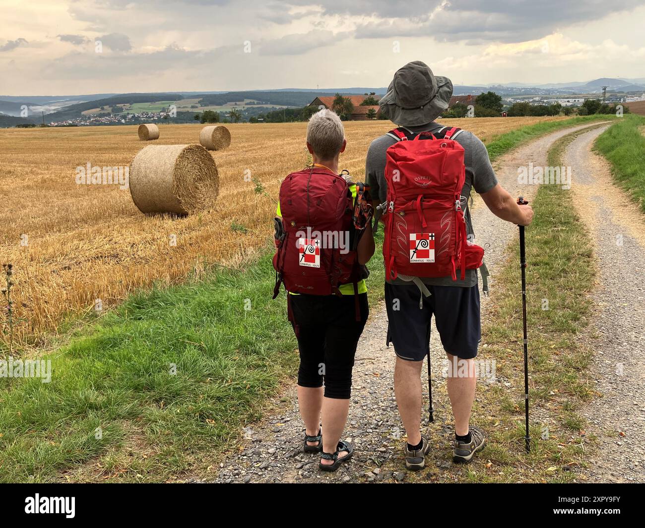 PRODUCTION - 07 août 2024, Hesse, Großenlüder : randonneurs Alexandra et Dirk Hosenfeld marchent le long de la route Bonifatius près de la chapelle Schnepfenkapelle en Hesse orientale. Les deux randonneurs ont le badge Bonifatius route attaché à leur sac à dos. La vue sur la région de Fulda et le Rhön s'ouvre depuis la colline. La dernière étape de la route Bonifatius commence ici. Alexandra et Dirk Hosenfeld ont parcouru toute la route de Mayence à Fulda il y a quelques années et aiment encore marcher quelques étapes du chemin de pèlerinage. Photo : Michael Bauer/dpa Banque D'Images