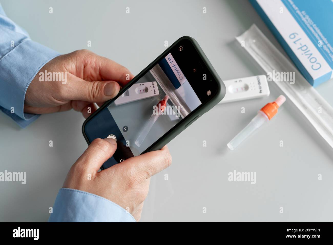 Mains féminines faisant une photo du kit d'auto-test avec un résultat positif covid 19 avec une caméra phoner à envoyer à un médecin. Kit de support d'auto-test Banque D'Images