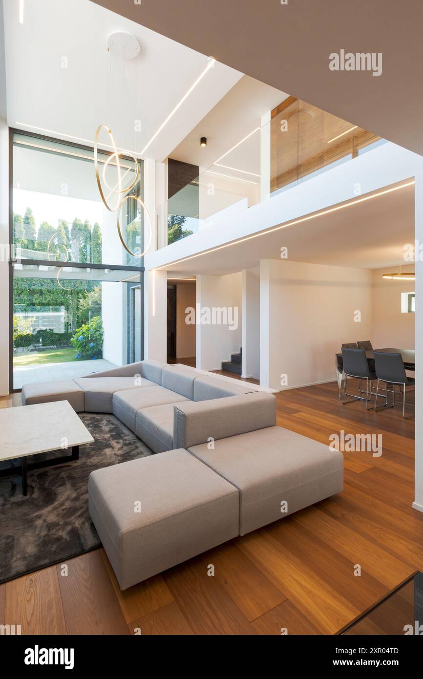 Salon moderne avec grand canapé, pouf, table basse centrale, au-dessus d'un grand tapis. Intérieur d'une maison moderne sur deux niveaux, personne à l'intérieur Banque D'Images