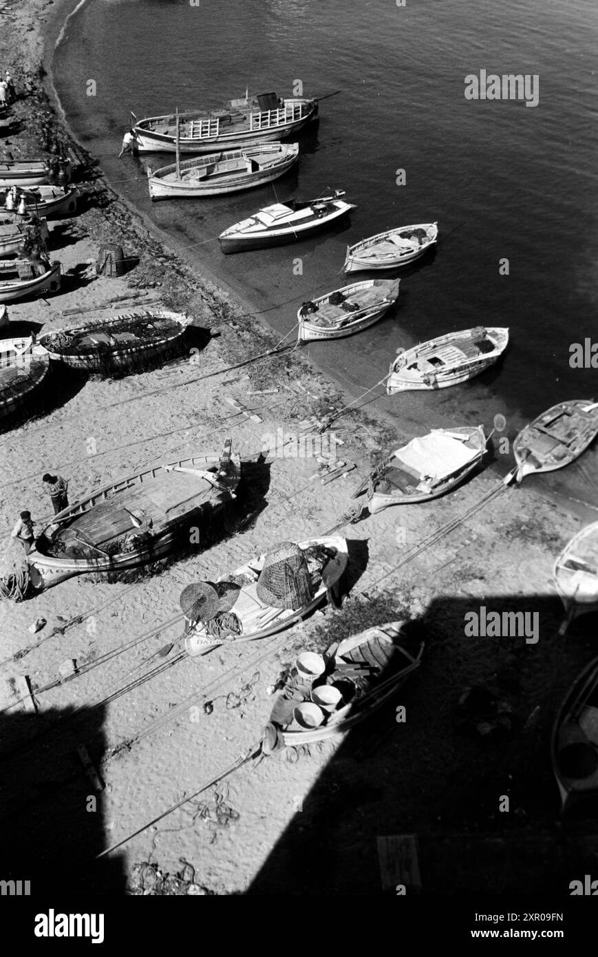 Fischerboote liegen am Strand von L'Escala in der sonne, während Männer, vermutlich Fischer, gehen ihrem Tagewerk nach, Costa Brava 1957. Les bateaux de pêche sont au soleil sur la plage de L'Escala, tandis que les hommes, probablement des pêcheurs, vaquent à leurs affaires quotidiennes, Costa Brava 1957. Banque D'Images