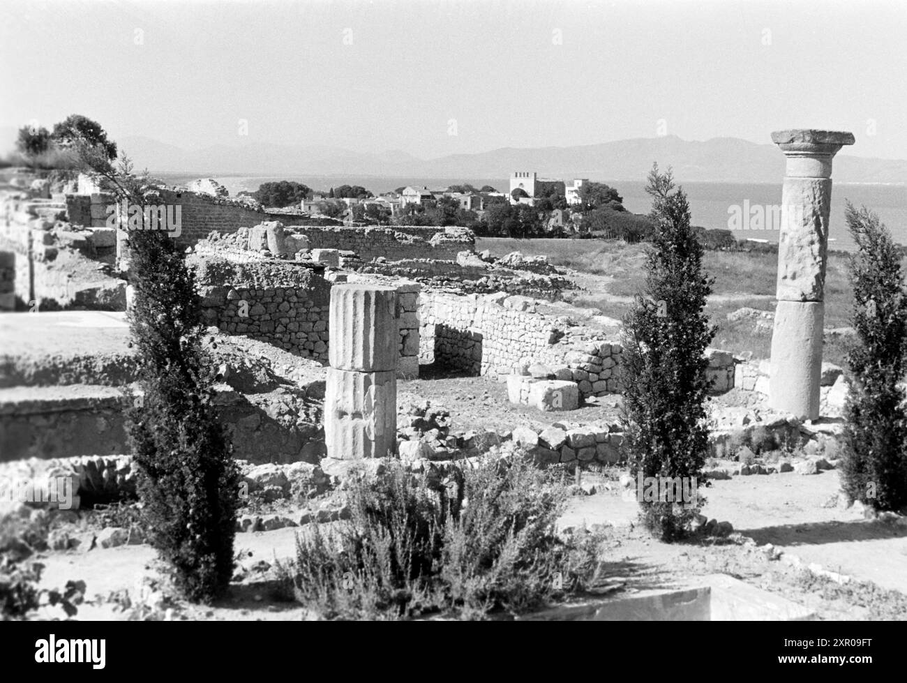 Reste von Mauern und dorischen Säulen zeichnen die Neapolis, den neueren griechisch-iberischen Teil von Empúries, aus, im Hintergrund ist die Església de Sant Martí sowie der Golf de Roses erkennbar, Costa Brava 1957. Des vestiges de murs et de colonnes doriques caractérisent la Neapolis, la nouvelle partie grecque-ibérique de Empúries, avec l'Església de Sant Martí et le golfe de Roses visibles en arrière-plan, Costa Brava 1957. Banque D'Images