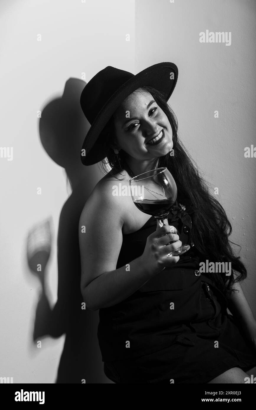 Portrait noir et blanc de belle femme en chapeau tenant un verre de vin. Prise de vue en studio Banque D'Images