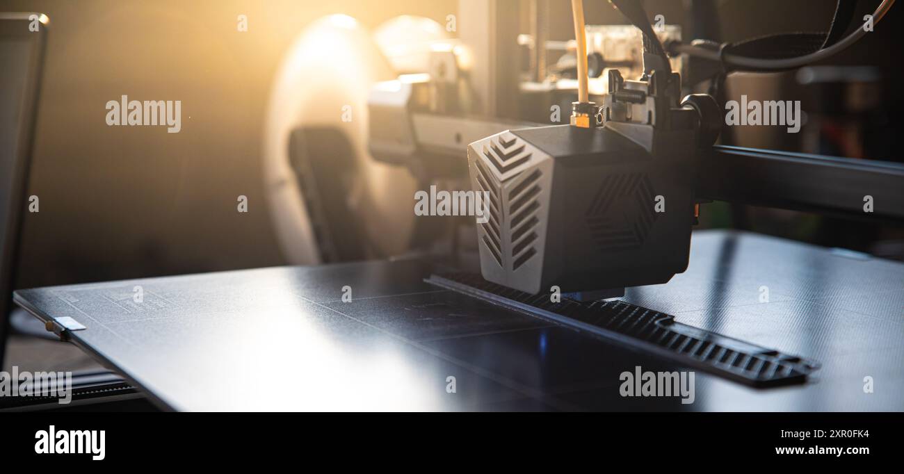 Imprimante 3D au travail avec un espace vide visible sur la gauche pour ajouter du texte. La lumière du soleil crée un éclairage dynamique, mettant l'accent sur la technol moderne de l'impression 3D. Banque D'Images