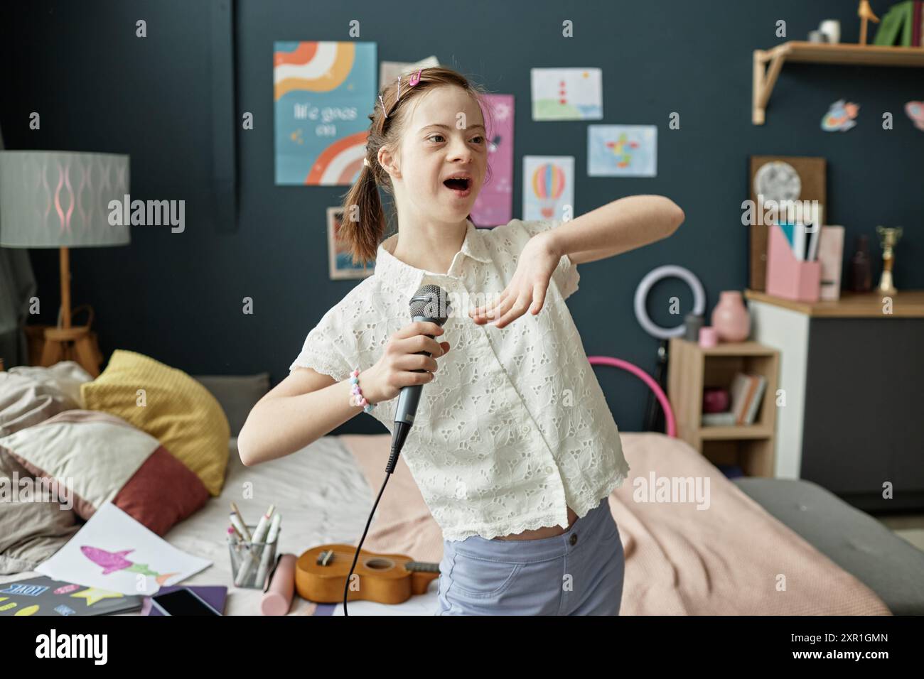 Jeune fille joyeuse tenant un micro et chantant dans sa chambre remplie d'affiches d'art et de livres éparpillés, dépeignant une atmosphère énergique et animée Banque D'Images