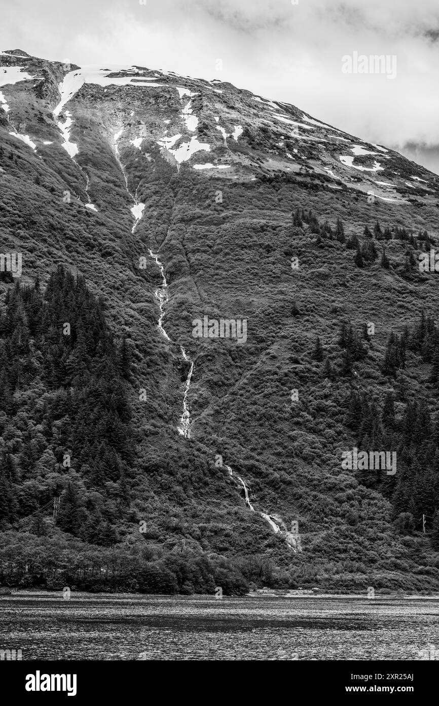 Petite chute d'eau descendant du sommet de la montagne couverte de neige dans la forêt et descendant vers la mer. Noir et blanc. Banque D'Images