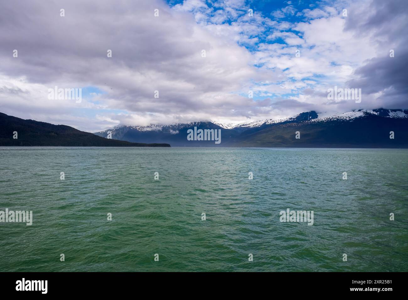 Ciel bleu avec des nuages blancs, des montagnes enneigées et une mer vert sarcelle. Banque D'Images