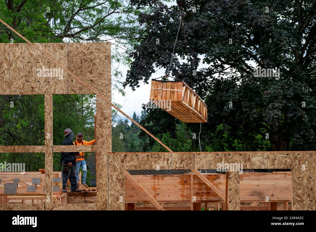 Construction de maison résidentielle, grue à flèche soulevant la livraison de bois, poutres de ferme de soutien en bois, à l'ouvrier d'attente Banque D'Images