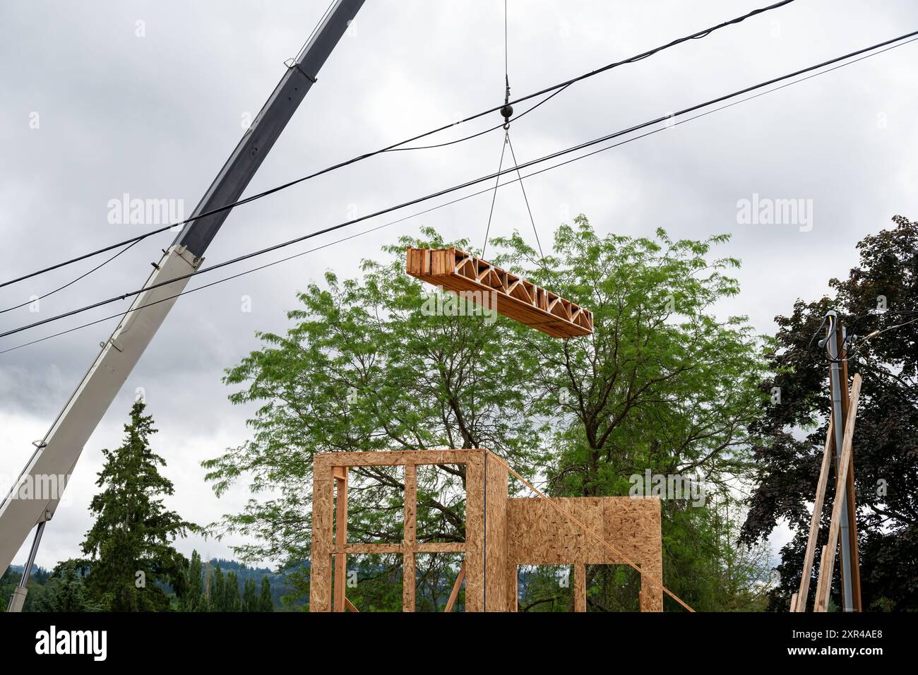 Construction de maison résidentielle, grue à flèche soulevant la livraison de bois, poutres de ferme de soutien, à l'étage suivant du projet Banque D'Images