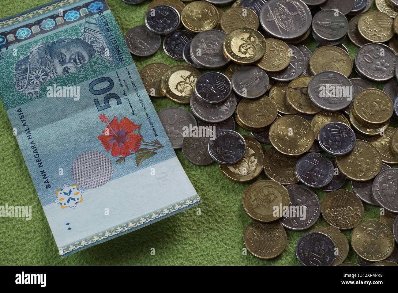 Terengganu, Malaisie - 24 août 2024 : gros plan de pièces de monnaie malaisiennes dispersées et de 50 ringgits d'argent malaisien sur fond vert Banque D'Images