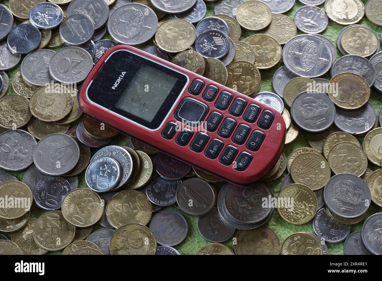 Terengganu, Malaisie - 24 août 2024 : gros plan de téléphones nokia rouges à clavier sur des pièces de monnaie malaisiennes dispersées Banque D'Images