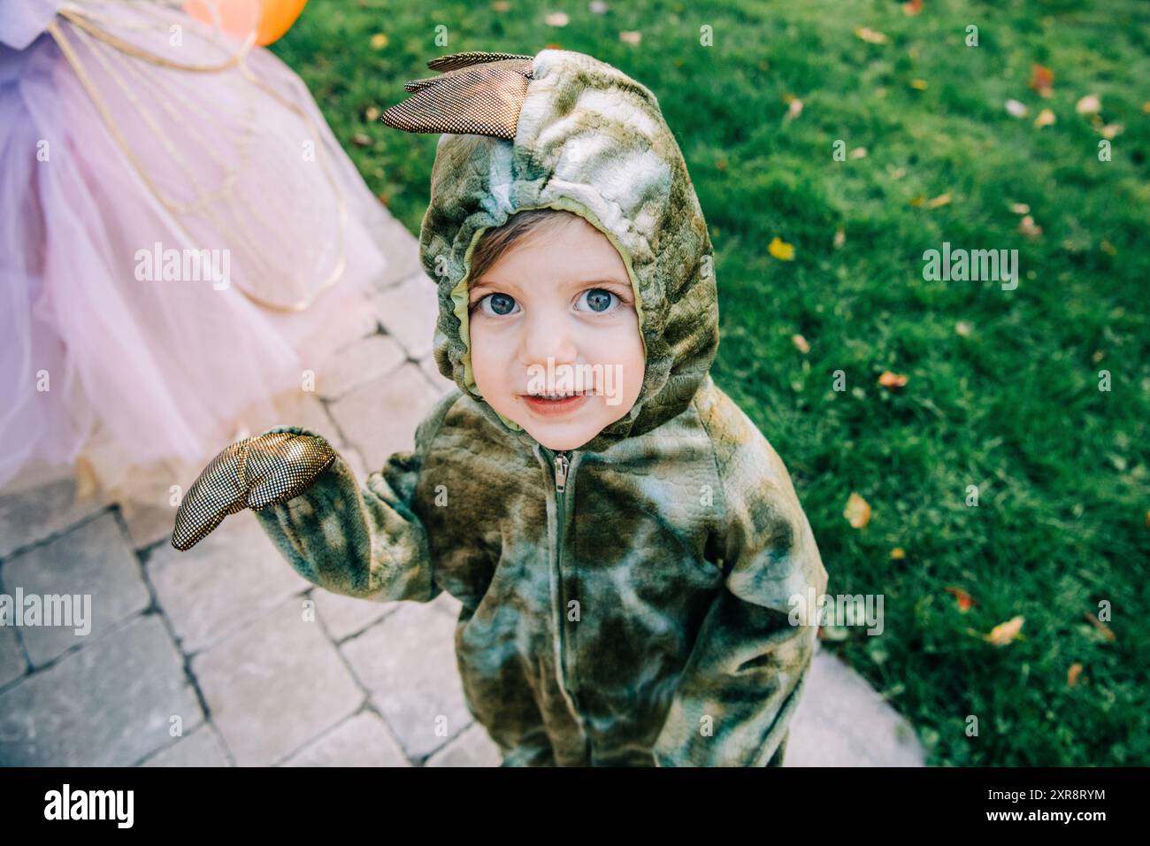 Enfant en bas âge dans un costume de dinosaure vert souriant à l'extérieur Banque D'Images