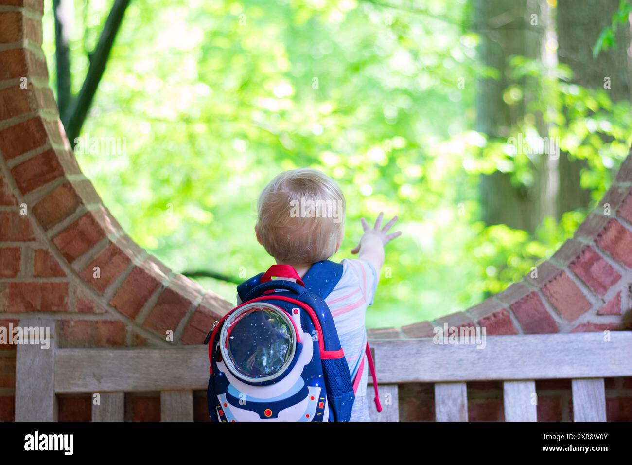 Enfant en bas âge avec sac à dos astronaute points à la nature à travers la ronde b Banque D'Images