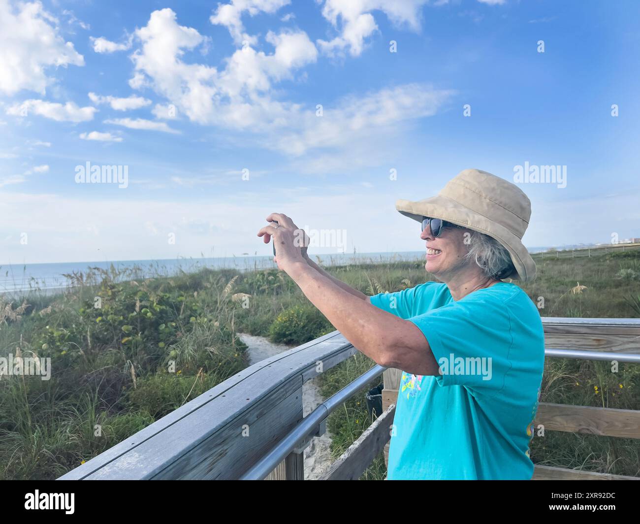 Femme souriante dans un chapeau de soleil prenant une photo à un boa côtier pittoresque Banque D'Images