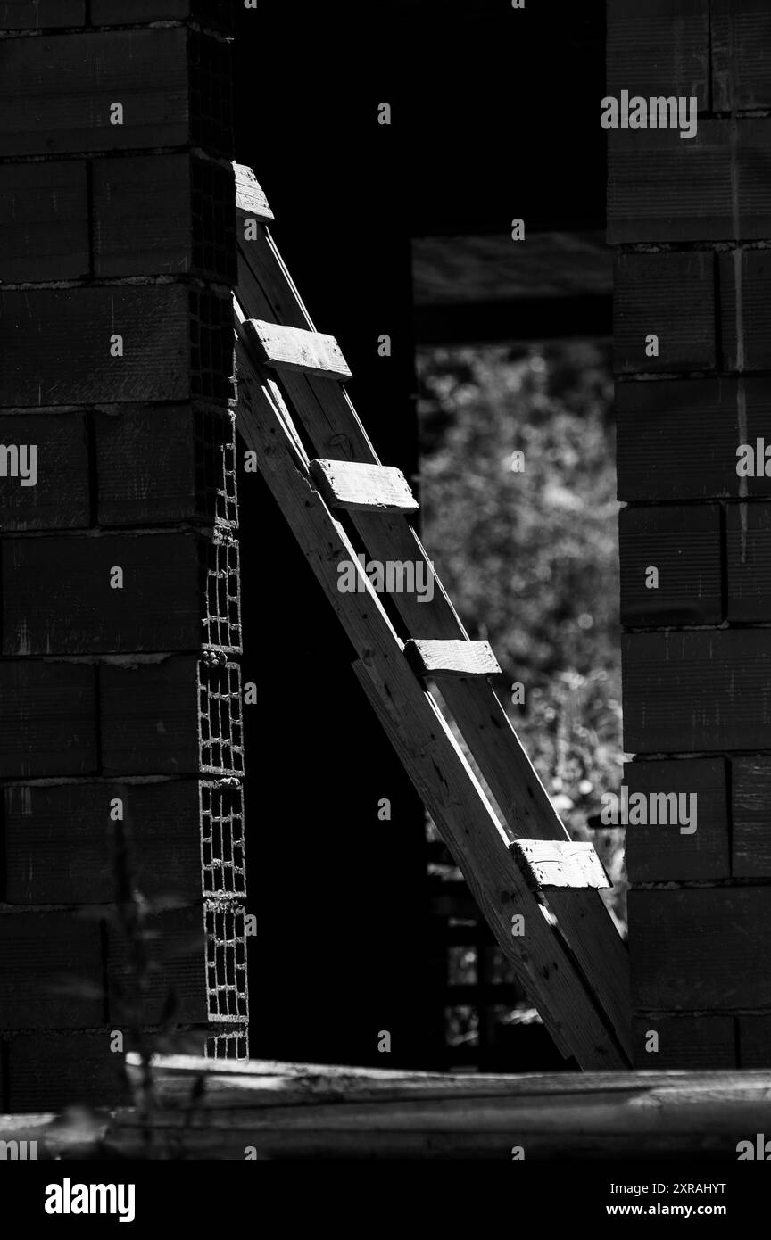Échelles en bois éclairées par le soleil, encadrées par une maison de construction inachevée. Noir et blanc.Monochrome. Banque D'Images