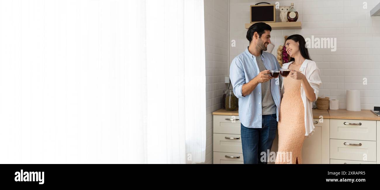 Romantique jeune couple cuisinant ensemble dans la cuisine ayant un bon moment ensemble. Jeune homme souriant tenant une tasse de café tandis que la petite amie est assise sur ki Banque D'Images