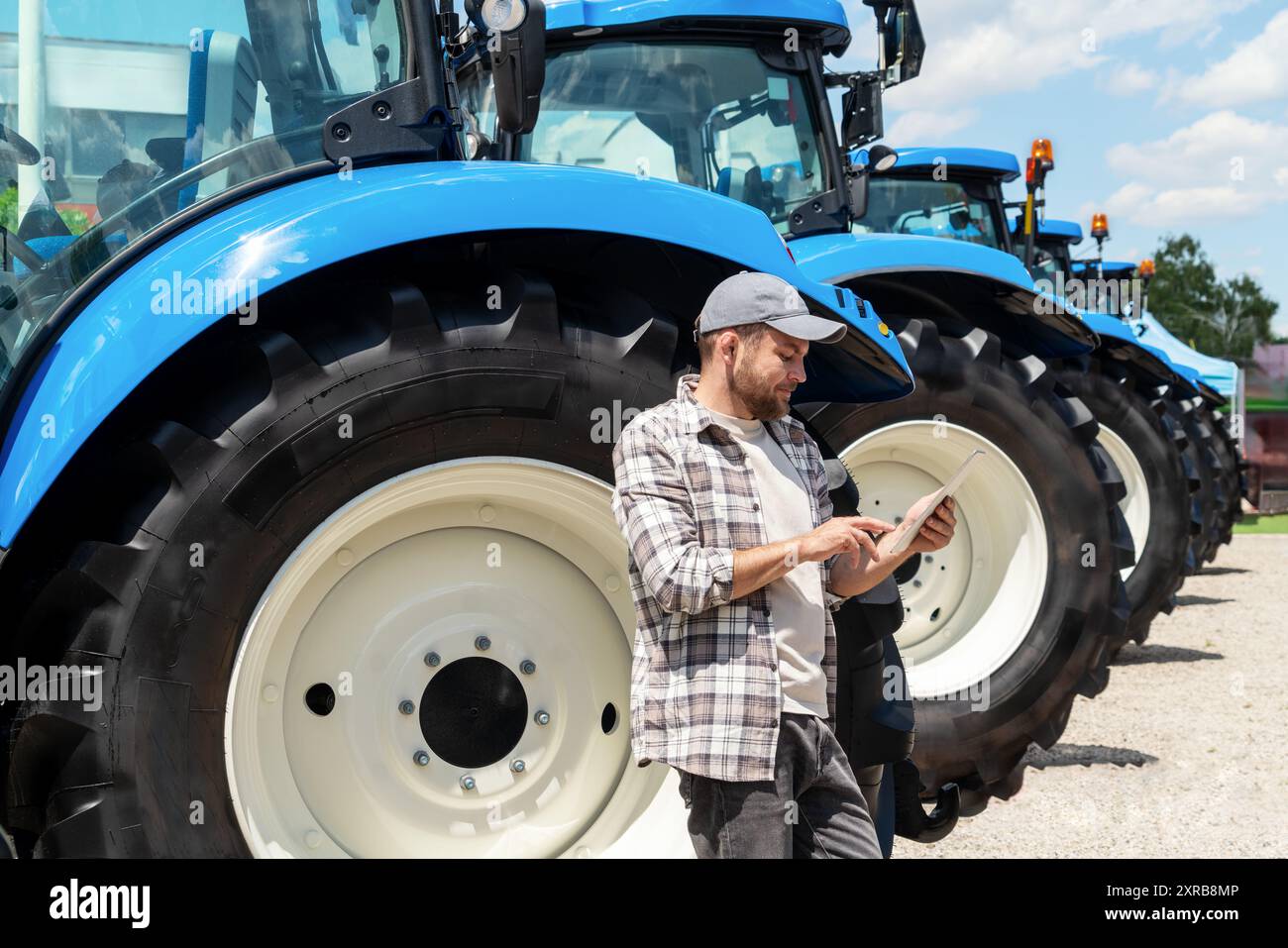 Concessionnaire de matériel agricole. Agro-industrie. Homme appuyé sur une roue de tracteur et utilisant une tablette numérique. Banque D'Images