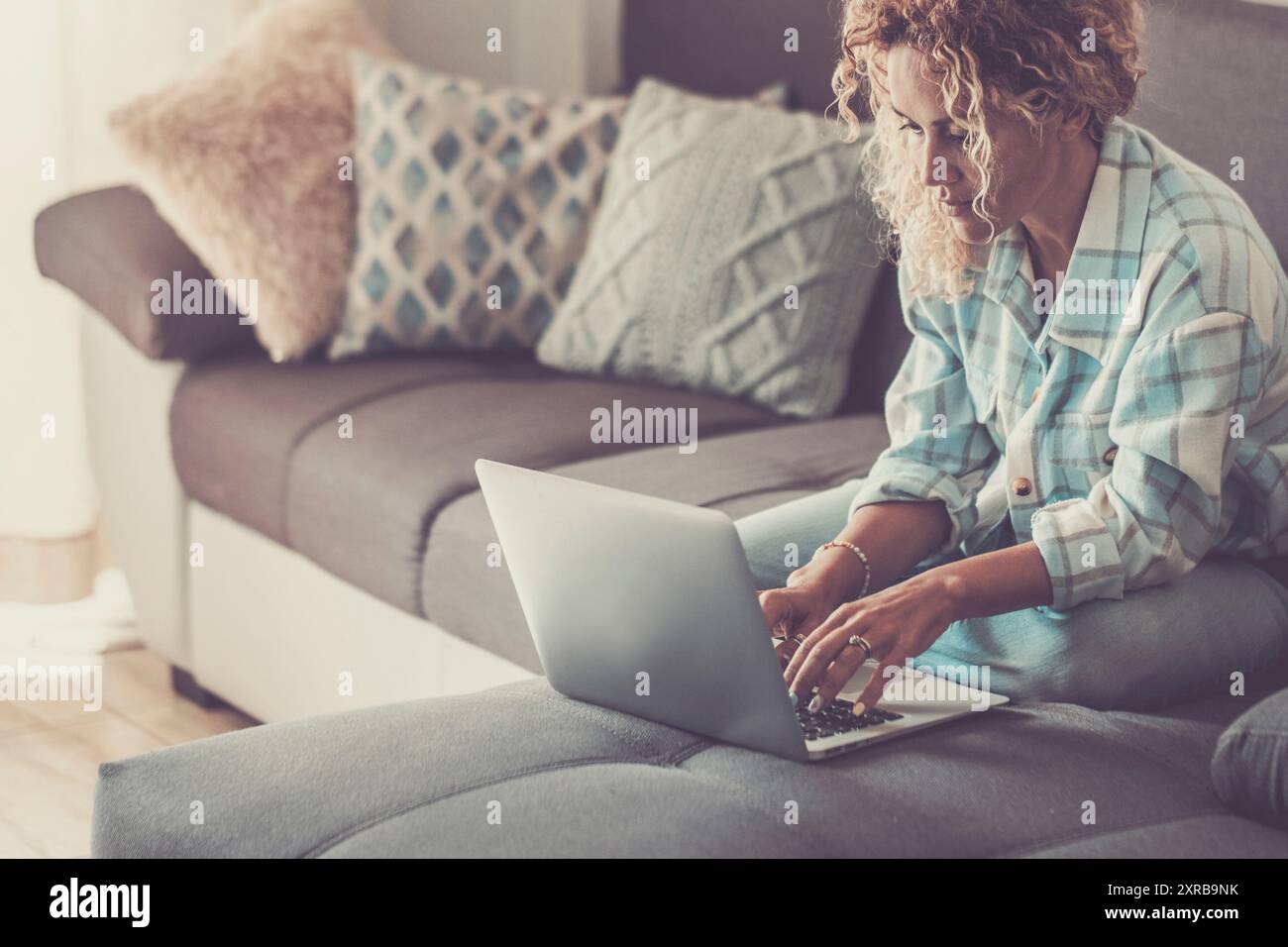 Une femme adulte utilisant un ordinateur portable sur le canapé. Technologie intérieure activité de loisirs en ligne. Les femmes modernes vivant seules et communiquent avec l'ordinateur de connexion sans fil. Dame de style de vie de travail intelligent Banque D'Images