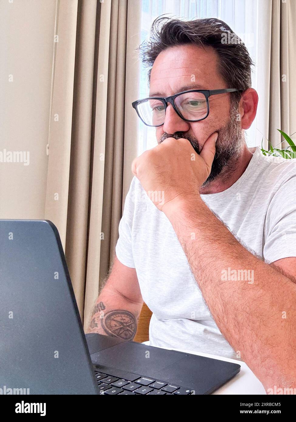 Un homme assis à la table travaillant sur ordinateur portable naviguant sur le net pour les activités de loisirs d'intérieur de petite entreprise seul. voyageur utilisant un ordinateur dans une suite luxueuse de l'hôtel. Fond lumineux de fenêtres lumineuses Banque D'Images