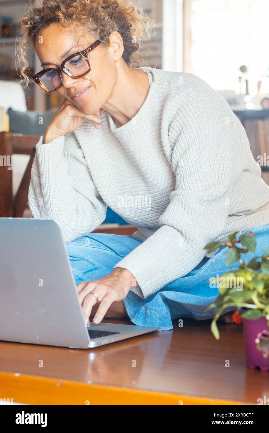 Une femme adulte travaillant sur un ordinateur portable seule à la maison assise sur le plancher en bois. Connexion et technologie sans fil. Les femmes modernes utilisant l'ordinateur pour rechercher le Web et faire des achats en ligne sur Internet Banque D'Images