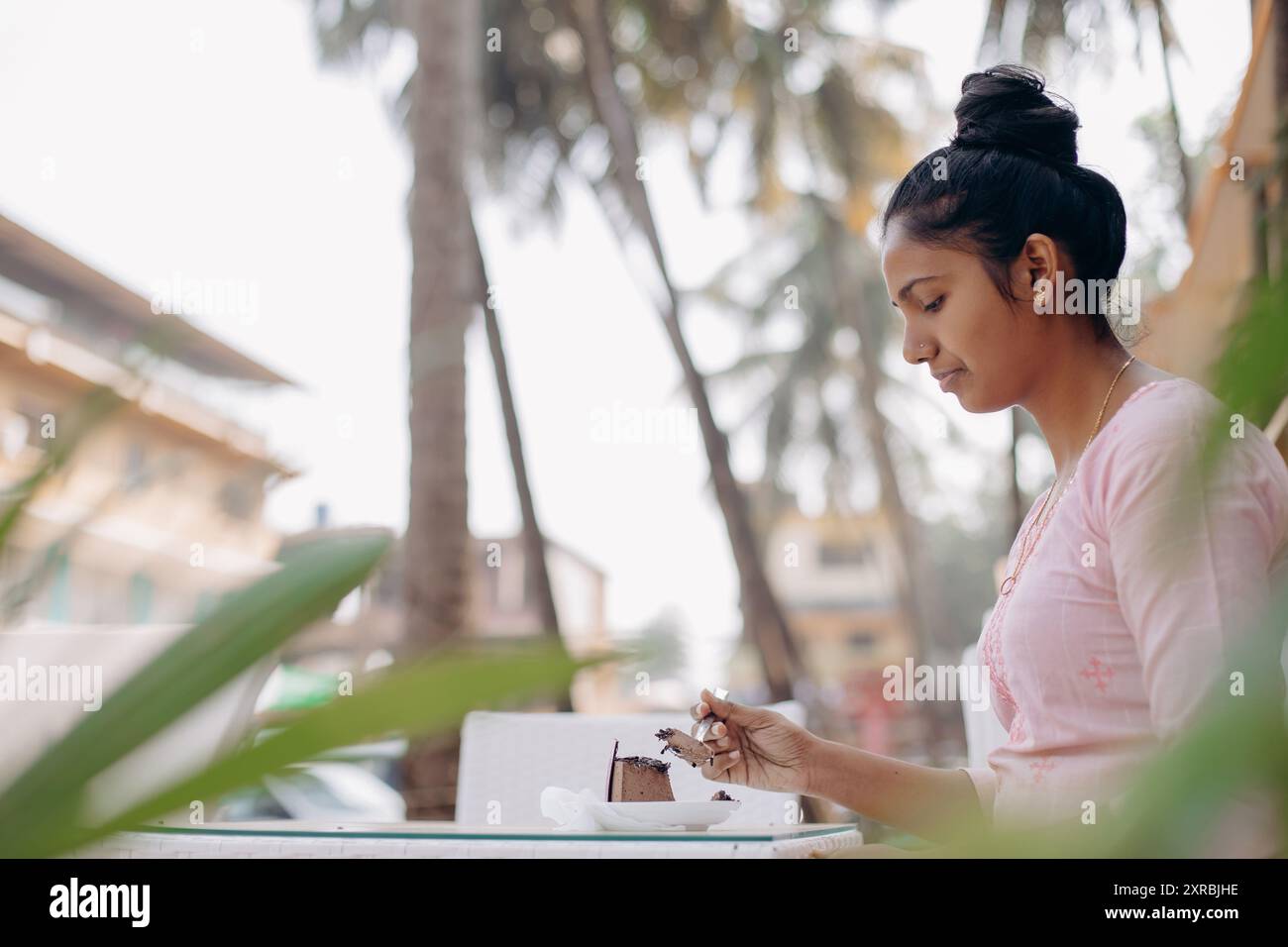 Petit déjeuner, déjeuner à l'air frais. Jeune femme indienne aime le dessert sucré, s'assoit à table dehors. Banque D'Images