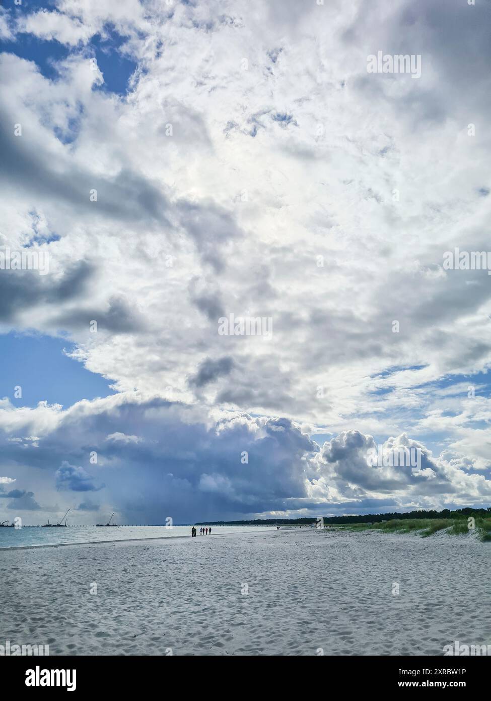 Les vacanciers loin de là marchent sur la plage et expérimentent l'atmosphère du soir avec le ciel nuageux spectaculaire après le coucher du soleil au bord de l'eau dans le Balt Banque D'Images