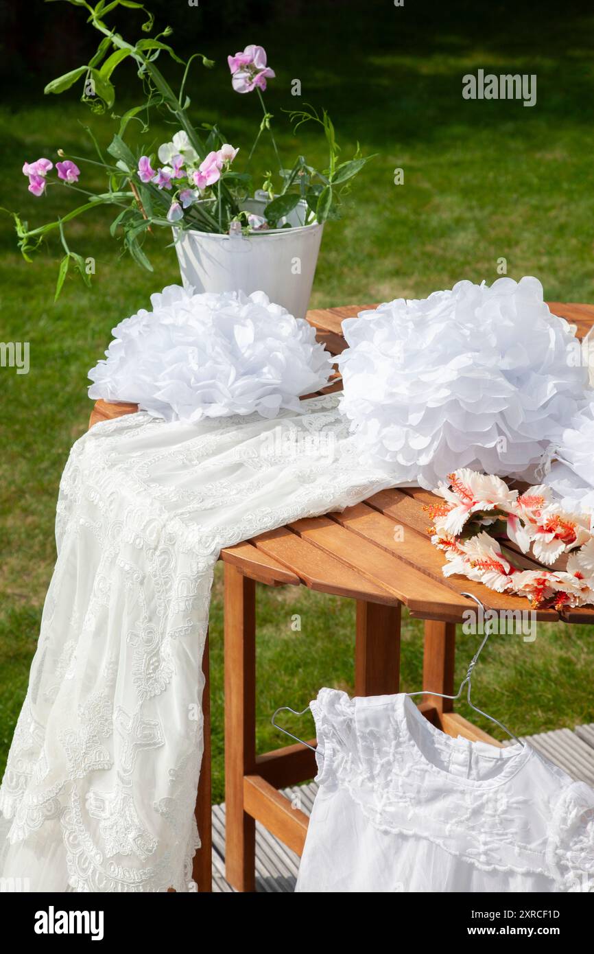 Table en bois dans le jardin avec robe pour enfants et fleurs, préparations pour un mariage, préparation de mariage en plein air Banque D'Images