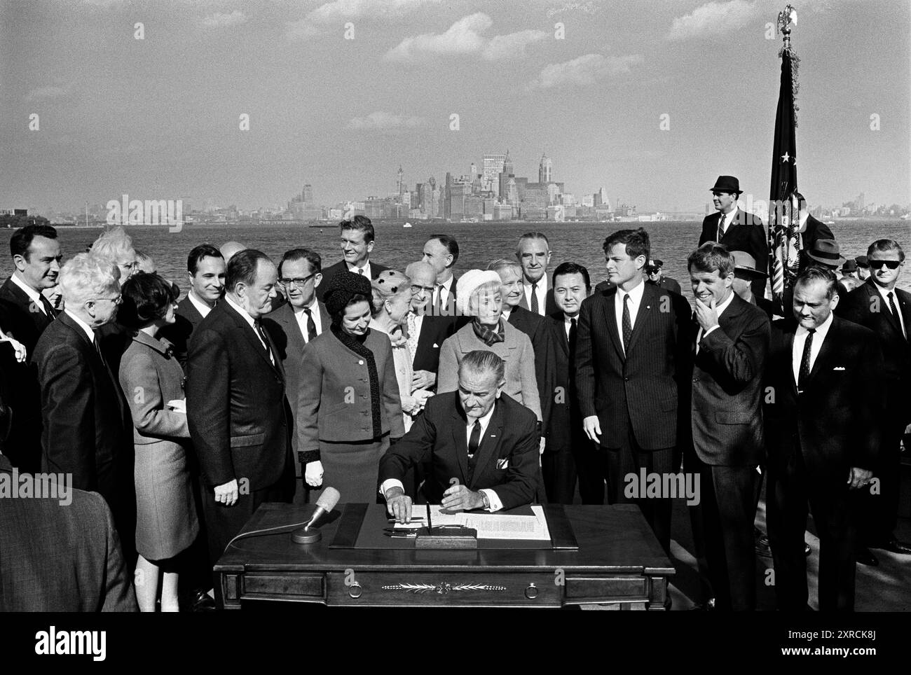 Le président américain Lyndon B. Johnson signant l'Immigration and Nationality Act de 1965 en tant que vice-président américain Hubert Humphrey, Lady Bird Johnson, Muriel Humphrey, sénateur Edward Kennedy sénateur Robert Kennedy, et d'autres regardent sur Liberty Island, New York City, New York, États-Unis, Yoichi Okamoto, 3 octobre 1965 Banque D'Images