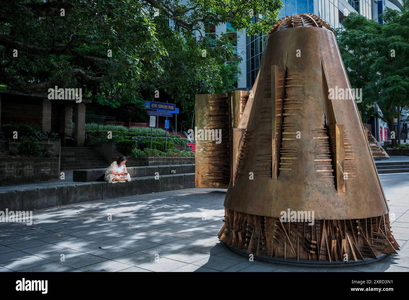 Une femme s’assoit à vapoter les jambes croisées et regarde son téléphone dans un espace public profitant de sa solitude à côté du travail artistique d’Arnaldo Pomodoro. Banque D'Images