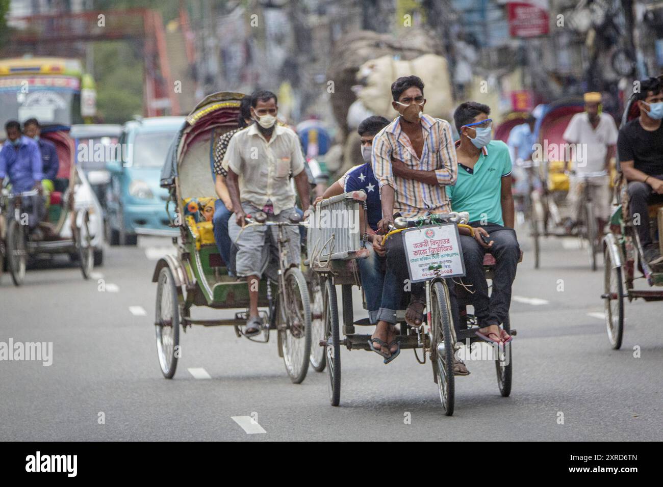 Un ricksha-wala, ou un conducteur de pousse-pousse avec ses passagers dans les rues de Dhaka. Les résidents de la capitale du Bangladesh, Dhaka, s'adaptent à la menace du virus corona COVID 19. Banque D'Images