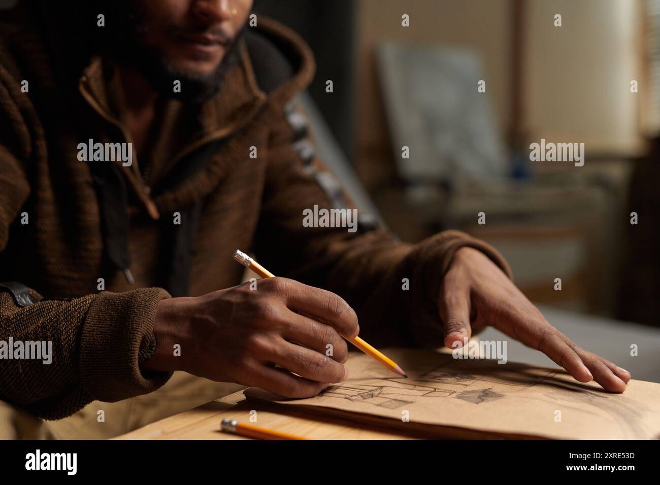 Gros plan des mains d'un artiste esquissant des idées de conception sur papier dans un cadre de studio d'art, tenant un crayon avec une concentration concentrée, entouré de matériaux artistiques Banque D'Images