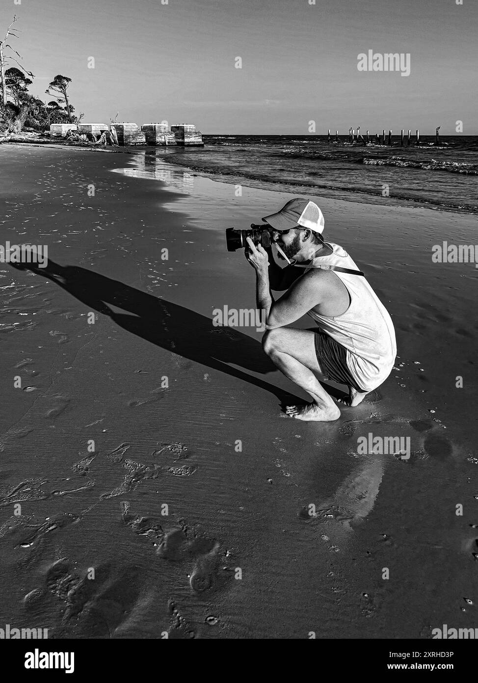 Photographe masculin attrayant capturant le coucher de soleil sur la plage dans une tenue décontractée et pieds nus Banque D'Images