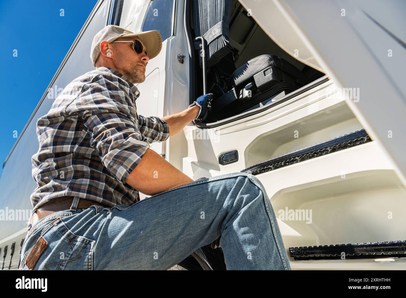 Professionnel Euro Trucker en lunettes de soleil grimpant dans un semi Truck moderne pendant une journée ensoleillée. Thème de l'industrie des transports. Banque D'Images