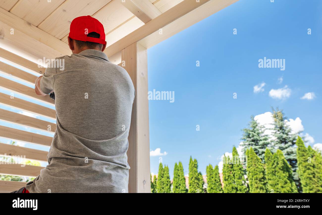 Un ouvrier sécurise les stores en bois tout en profitant du soleil éclatant et d'un ciel bleu clair dans un cadre extérieur. Banque D'Images