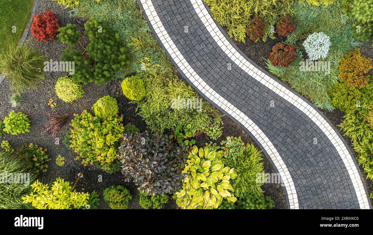 Un jardin serein rempli de diverses plantes et arbustes crée une toile de fond colorée pour un sentier sinueux. Banque D'Images