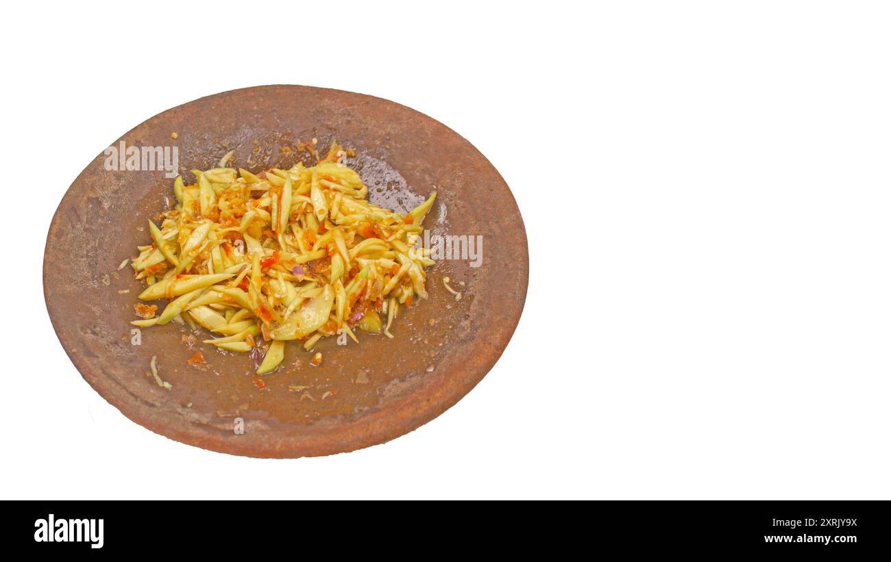 Sambal Mangga ou sauce Chili mélangée à de jeunes fruits de manggo tranchés servir sur un mortier traditionnel et un pilon isolé. Authentique typique de In Banque D'Images