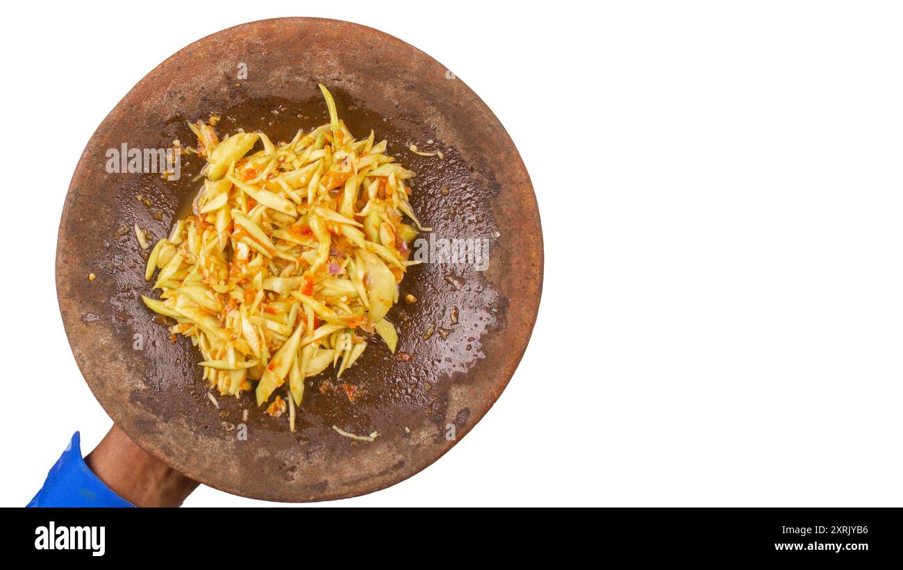 Sambal Mangga ou sauce Chili mélangée à de jeunes fruits de manggo tranchés servir sur un mortier traditionnel et un pilon isolé. Authentique typique de In Banque D'Images
