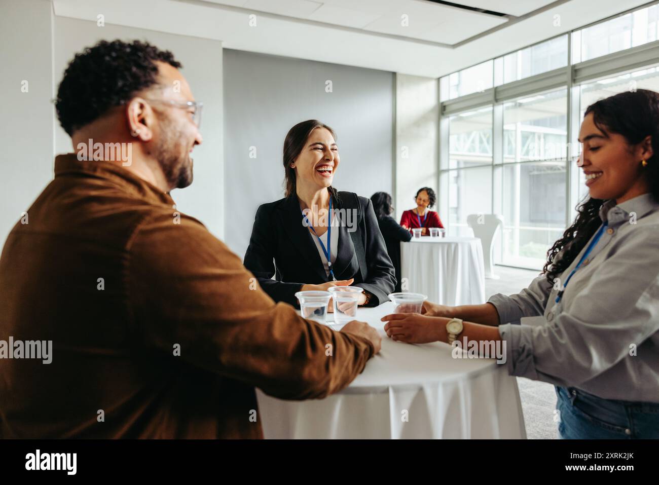 Groupe de collègues réseautant et partageant des rafraîchissements pendant une pause conférence, profitant de rires et de conversations informelles. Banque D'Images