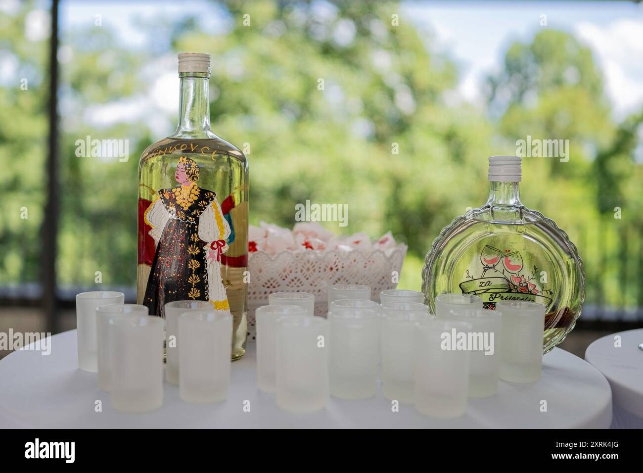 , Deutschland, 10.08.2024, Zwei traditionelle Schnapsflaschen und mehrere Gläser stehen auf einem weißen Tisch im Freien, Bereit für eine Verkostung. Banque D'Images